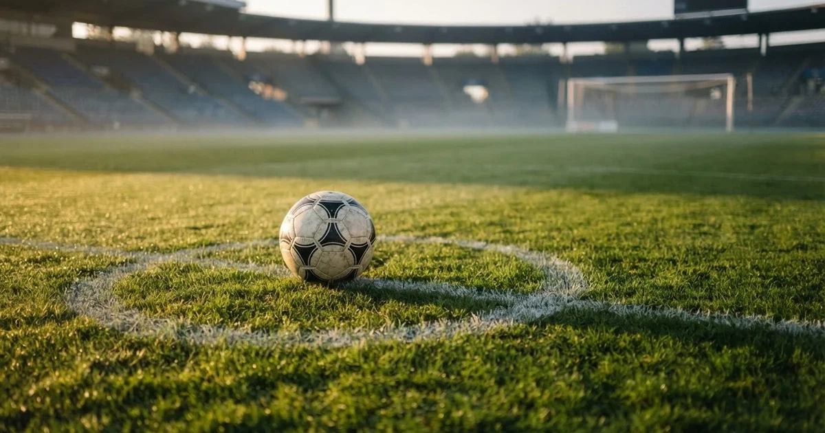 Een voetbal op de middenstip van een grasveld in het ochtendlicht