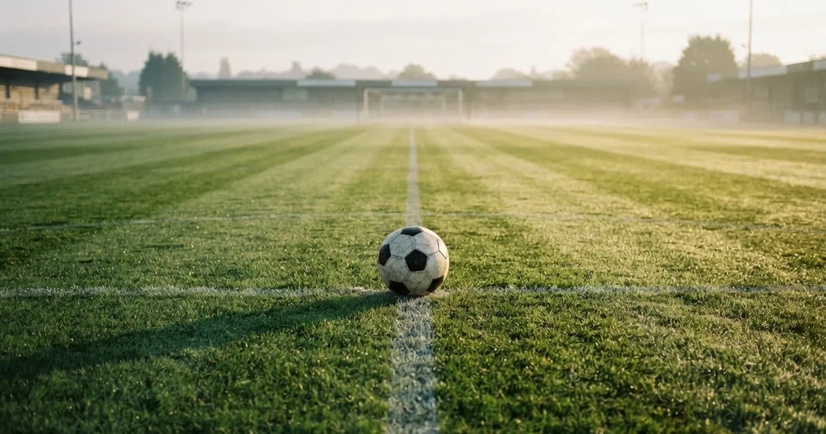 Een voetbal op de middenstip van een grasveld in het ochtendlicht