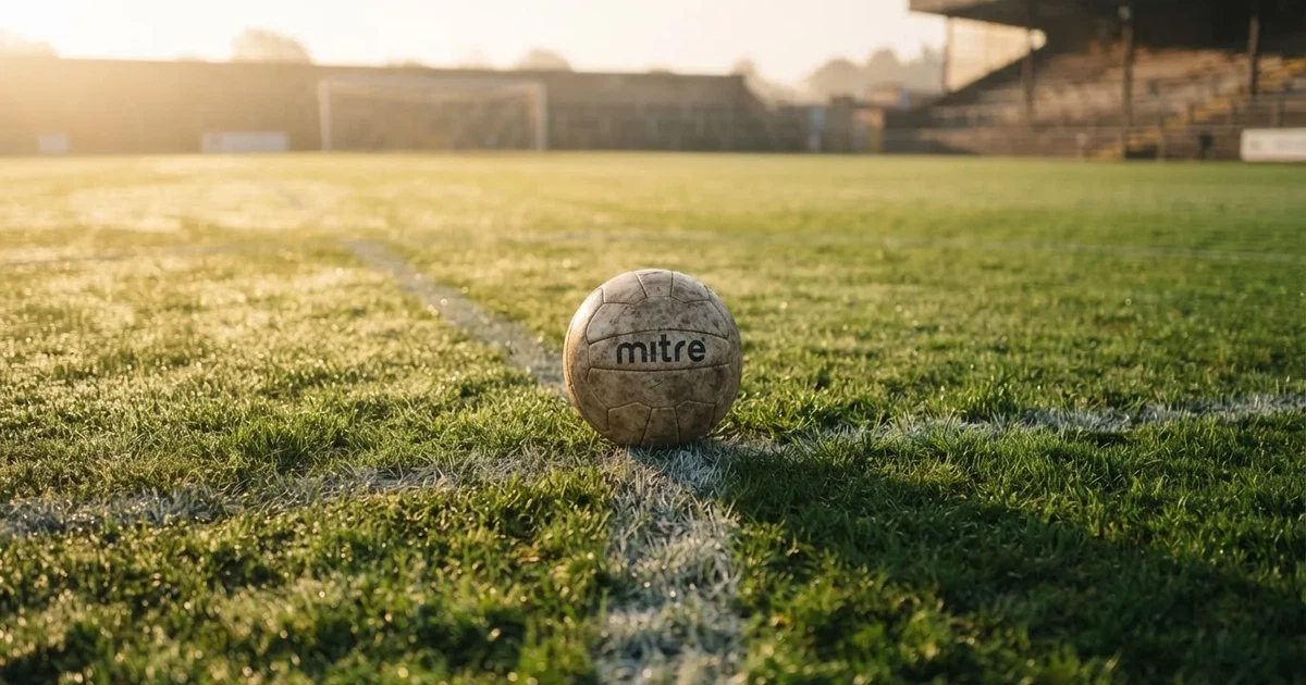 Een voetbal op de middenstip van een grasveld in het ochtendlicht