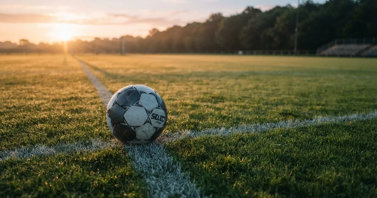 Een voetbal op de middenstip van een grasveld in het ochtendlicht
