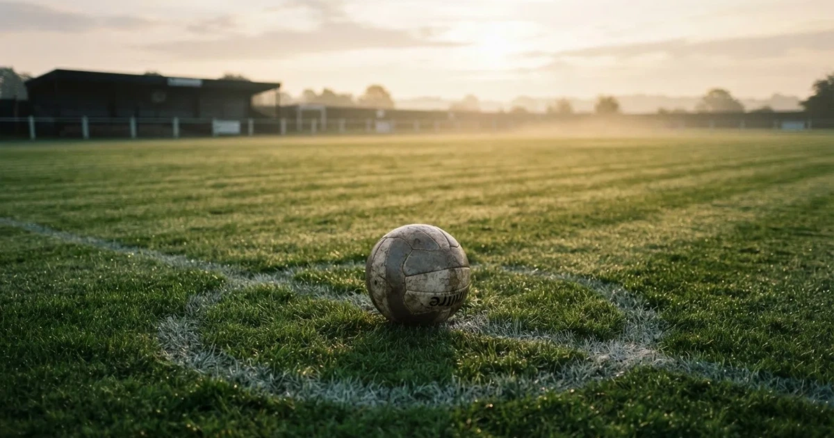Een voetbal op de middenstip van een grasveld in het ochtendlicht