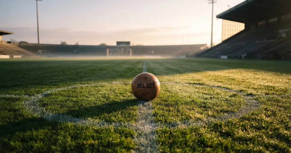 Een voetbal op de middenstip van een grasveld in het ochtendlicht
