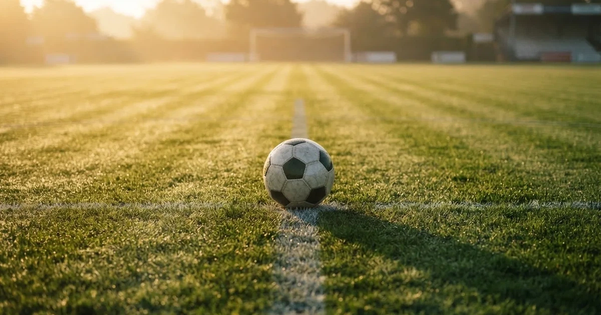 Een voetbal op de middenstip van een grasveld in het ochtendlicht