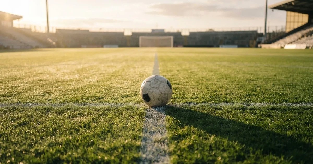 Een voetbal op de middenstip van een grasveld in het ochtendlicht